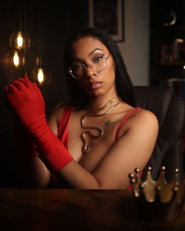 Hazel at her desk in red evening gloves and a gold snake necklace